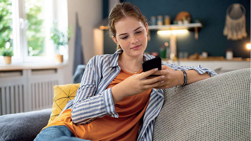 Frau, die auf dem Sofa sitzt und ein Mobiltelefon bedient